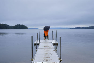 Rear view of man standing on pier over lake against sky