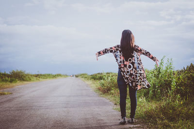 Rear view of woman standing by road against sky