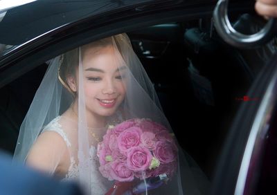 Happy bride with pink rose bouquet exiting car