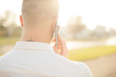 Young man talking on smart phone while standing against sky