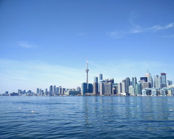 Cn tower and skyscrapers by river against blue sky