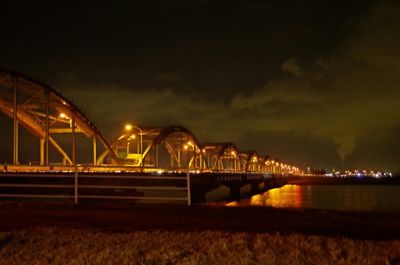 Illuminated bridge over water against sky at night