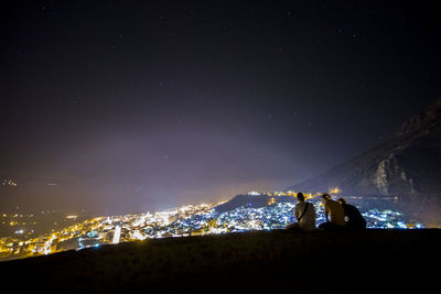 People standing on illuminated land against sky at night
