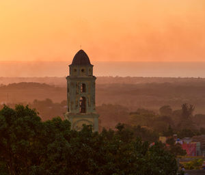 Scenic view of building by trees against orange sky