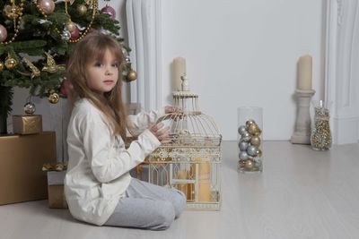 Side view of girl with birdcage on floor at home during christmas