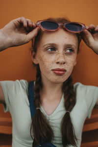 Girl with braided girl holding sunglasses while looking away
