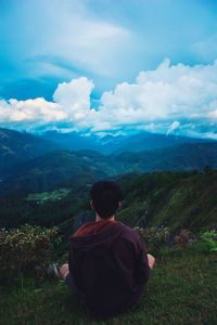 Rear view of man sitting on mountain against sky