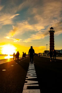 Silhouette people walking on road against sky during sunset