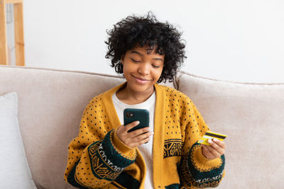 Young woman using mobile phone while sitting on sofa at home