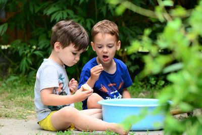 Brothers eating food while sitting on land