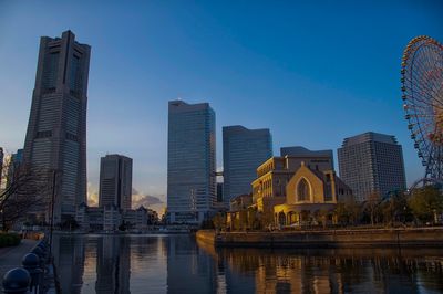 Modern buildings by river against sky in city