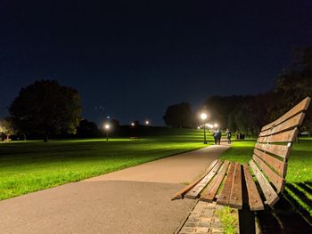 Empty park bench by street against sky at night