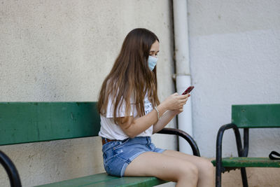 Woman using mobile phone while sitting on wall