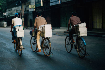 Rear view of newspaper vendors riding bicycles on road in city
