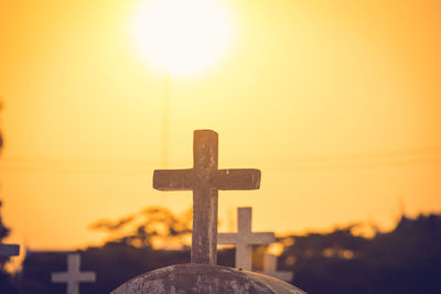 Cross in cemetery against sky during sunset