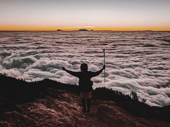 Rear view of man standing on sea shore against sky during sunset