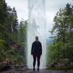 Rear view of woman standing against waterfall