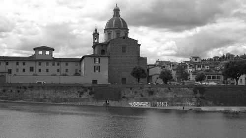 View of buildings by river against cloudy sky