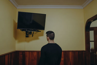 Rear view of boy standing against wall at home