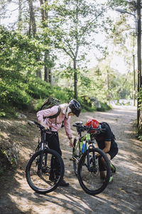 Senior woman talking to male friend repairing cycle on footpath