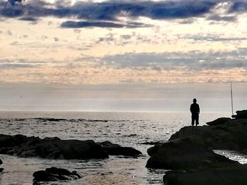 Silhouette man standing on rock at beach against sky
