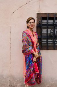 Portrait of smiling beautiful woman in traditional cloths standing against wall