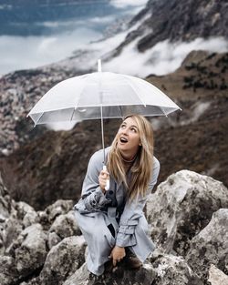 Portrait of a young woman standing on rock with umbrella 