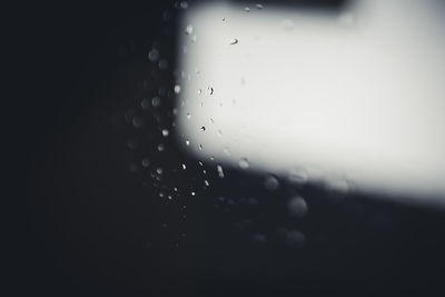 Close-up of wet glass window against black background