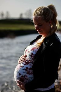 Smiling pregnant woman standing at lake