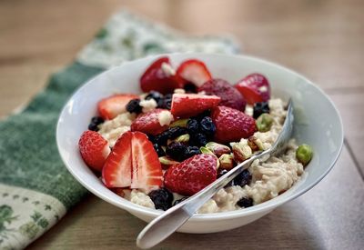 Close-up of oatmeal with fruits and pistachios in bowl on table.