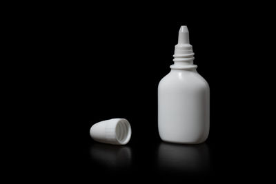 Close-up of white bottle on table against black background