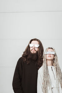 Young couple wearing sunglasses standing against wall