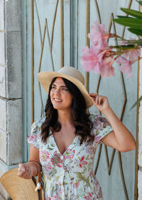 Portrait of beautiful girl wearing floral pattern dress and hat, posing under oleander flower