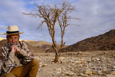 Portrait of senior man sitting on mountain against sky