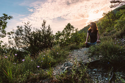 Rear view of woman on rock amidst trees against sky