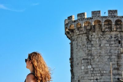 Low angle view of woman with castle in background against blue sky