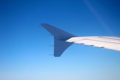 Low angle view of airplane wing against clear blue sky