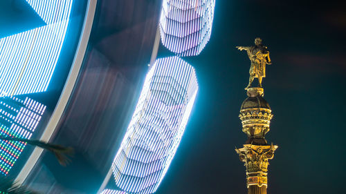 Colorful illuminated ferris wheel in night city landscape view and a monument statue