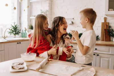 Mom, daughter and son laugh, have fun and communicate in the kitchen on christmas day