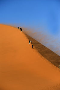 Men walking on sand dune against clear sky
