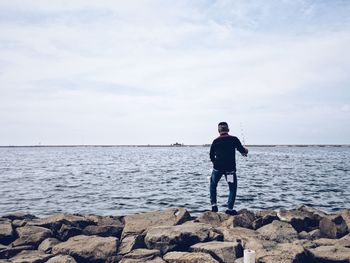 Rear view of man standing on shore against sea