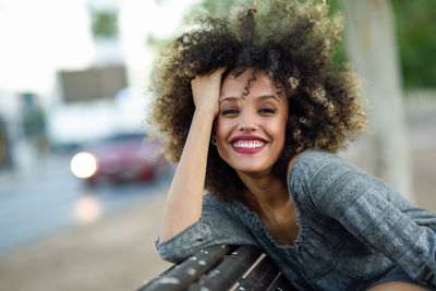 Portrait of smiling young woman sitting on bench in city