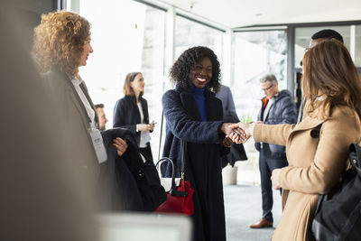 Smiling businesswoman shaking hand with female professional at seminar in convention center