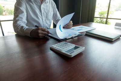 Midsection of man using mobile phone while sitting on table