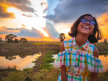 Portrait of smiling young woman standing against sky during sunset