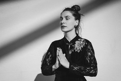 Young woman standing against wall meditating