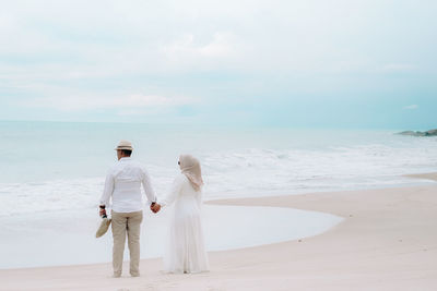 Rear view of woman standing at beach against sky