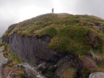 Man on rock by mountain against sky