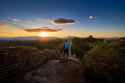 Rear view of person standing by great wall of china against sky during sunset