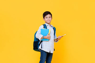 Portrait of smiling boy standing against yellow background
